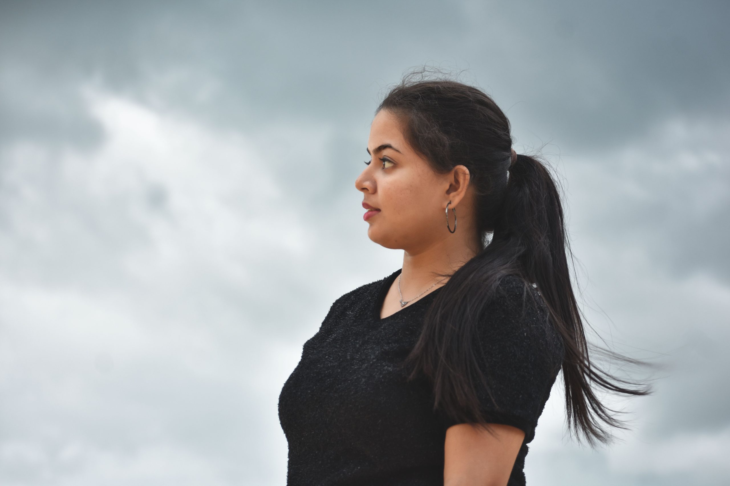 Profile portrait of a woman with ponytail against a cloudy sky in Bhubaneswar, India.